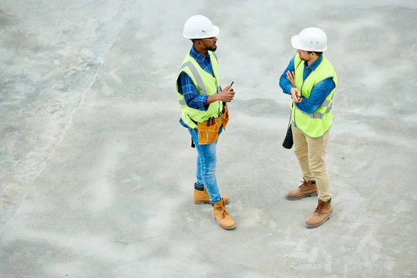 Side View Two Men Hardhats Waistcoats Standing Construction Site Talking — Stock Photo, Image