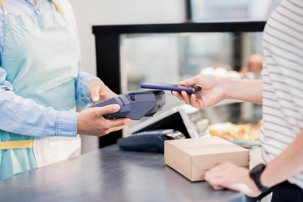 Mid section portrait of unrecognizable woman paying by smartphone  via NFC for her order in shop or cafe