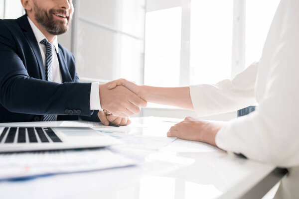 Close-up of satisfied business people sitting at table with papers and shaking hands after concluding contract, they starting partnership