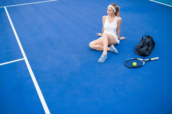 연습에서 휴식을 취하는 테니스 코트에서 바닥에 앉아있는 여자의 평면도 초상화 — 스톡 사진