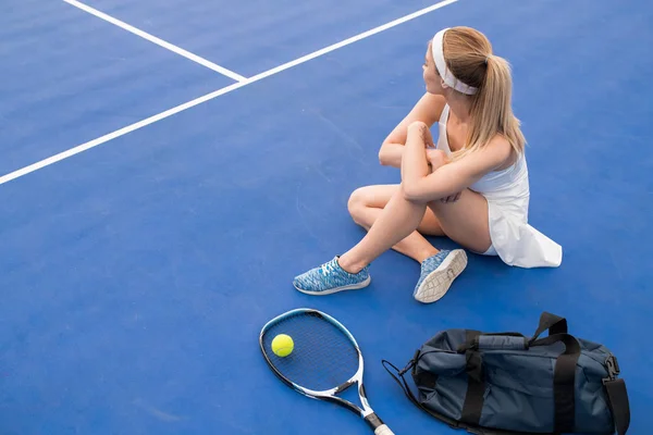 屋内テニスコートで床に座っている若いブロンドの女性の高アングルポートレート練習から休憩を取り スペースをコピー — ストック写真