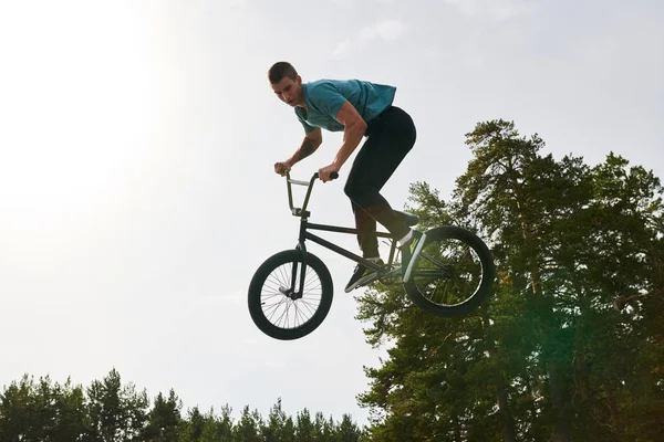 Full length portrait of muscular young man doing bmx stunts jumping up high against sky, copy space