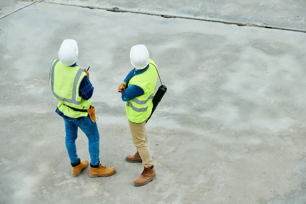 Vista Posterior Dos Hombres Cascos Chalecos Examinando Sitio Construcción Durante — Foto de Stock