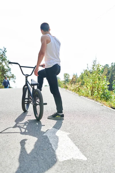 Full length back view portrait of muscular young man standing on hill  by bmx bike, copy space