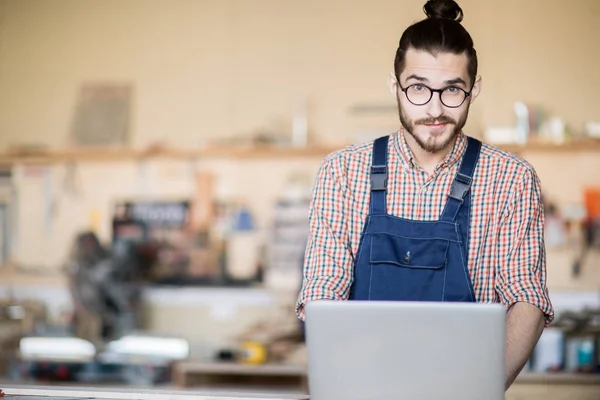 stock image Waist up portrait of young worker using laptop and looking at camera  standing at table in modern workshop, copy space