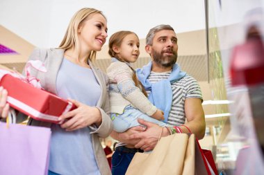 Küçük kızı ile rahat ebeveynlerin aşağıdan alışveriş merkezinde pencereye bakarak tatil alışveriş i