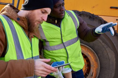 İş yerinde ağır sanayi kamyonunun yanında duran dijital tablet kullanan iki işçinin yan görünüm portresi, biri Afro-Amerikalı, kopyalama alanı