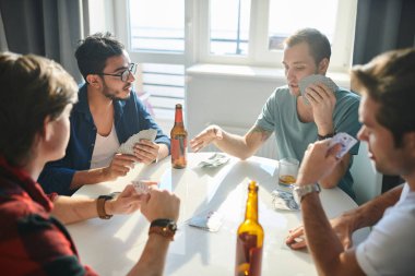 Bir grup erkek arkadaş masada kağıt oynuyor ve evde alkol içiyor
