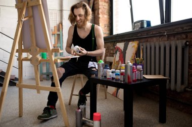 Sanat stüdyosunda iş keyfi yaparken şöne üzerinde yakışıklı uzun saçlı sanatçı boyama tam uzunlukta portre, kopya alanı