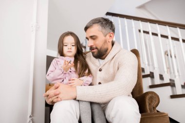 Evde deri koltukta oturan küçük kız ile oynayan olgun sakallı adam portresi