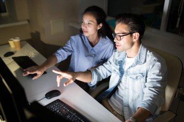 Gece geç saatlerde karanlık ofiste bilgisayar kullanırken ekrana işaret eden ve projeyi tartışan iki meslektaşının yüksek açılı portresi