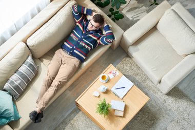 Above view portrait of pensive male psychologist relaxing after session while lying on  couch in sunlit office, copy space clipart