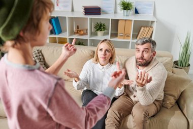 Hipster giyim sorunlu genç ebeveynlerin önünde duran ve onları lanet ederken orta parmak gösteren, şok anne silah silkme ve onun hoşnutsuzluğunu ifade