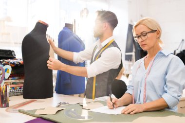 Güneş ışığıyla aydınlatılan atölyede çalışan moda tasarımcılarının portresi, olgun kadın çizim skeçleri ön planda odaklanmak, kopya alanı