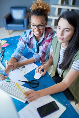 Modern ofiste masa başında çalışırken mutlu bir şekilde gülümseyen, biri Afrikalı iki yaratıcı genç kadının yüksek açılı portresi