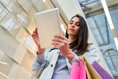 Sitenin görünümü aşağıda siyah saçlı çekici bayan alışveriş merkezi üzerinde yürüyüş ve tek başına alışveriş yaparken aynı anda tablet kullanarak konsantre