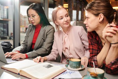 Kitap kullanarak sunuma hazırlanan ve kafede çay içerken dizüstü bilgisayar kullanarak internette gezinmeye hazırlanan bir grup üniversite öğrencisi