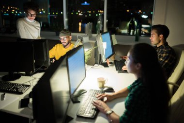 Açık ofiste gece geç saatlerde işyerlerinde bilgisayar kullanan çok ırklı insan grubu