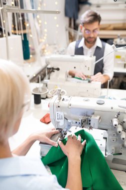 Atölye atölyesinde arka arkaya oturan dikiş makineleri kullanan terzilerin yüksek açılı portresi, fotokopi alanı