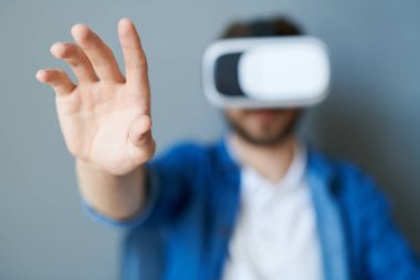 Oyun oynarken veya 360 video izlerken, uzayı kopyalarken, ön plana odaklanırken koltukta oturarak vr kıyafeti giyen modern genç adamın portresi