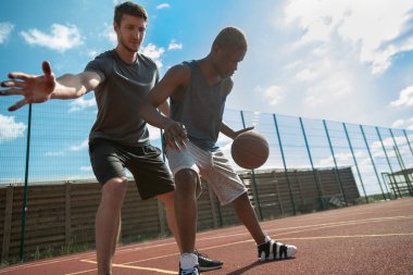 Güneş ışığı yla aydınlatılan açık havada basketbol oynayan iki yakışıklı genç adamın aksiyon çekimi, kopya alanı