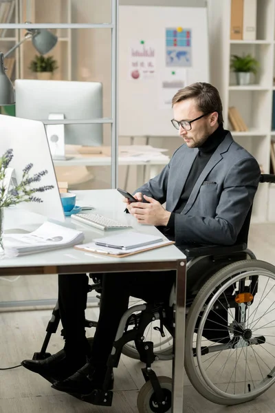 Poważny Pracownik Biurowy Siedzi Wózku Inwalidzkim Przy Stole Czyta Wiadomość — Zdjęcie stockowe