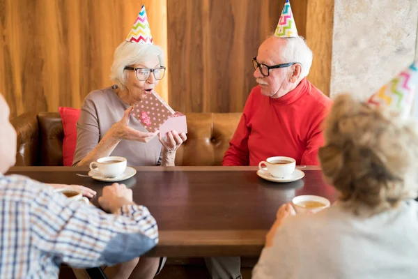 乔利兴奋的生日女士在党帽惊讶与礼物开幕礼物从朋友在她的党在咖啡馆 — 图库照片