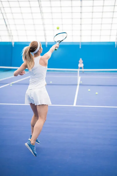 バックビューアクション屋内コートでの練習中のジャンプでラケットを振る女性のテニス選手の肖像画 コピースペース — ストック写真