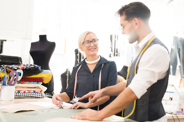 Güneş ışığı ile aydınlatılan atölyede çalışırken meslektaşı ile proje yi tartışan gülümseyen moda tasarımcısı portresi, kopya alanı