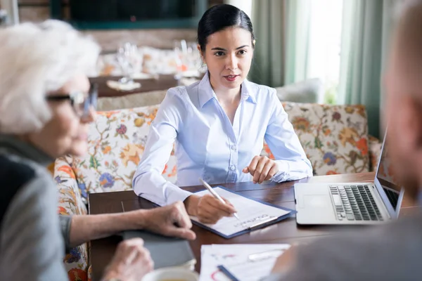 Young businesswoman sitting at meeting at cafe with her colleagues and signing a business contract