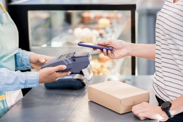 Side view mid section of unrecognizable woman paying by smartphone  via NFC for her order in shop or cafe