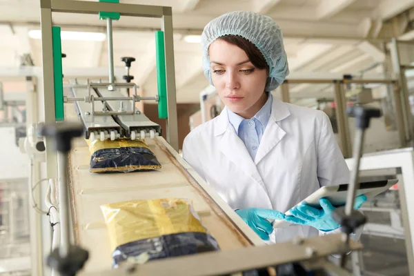 現代の食品工場で包装プロセスを制御し コンベアベルトを滑り落ちるマカロニバッグを見て若い女性の肖像画 コピースペース — ストック写真