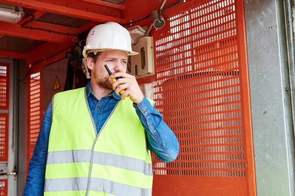 Waist up portrait of construction worker standing in elevator and speaking by walkie-talkie giving instructions to crew on site, copy space