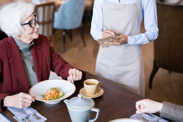テーブルの上にサラダを置いてレストランに座り 隣人に注文をするシニア女性 — ストック写真