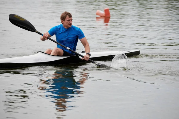 The athlete holding an oar and floating in kayak on the lake