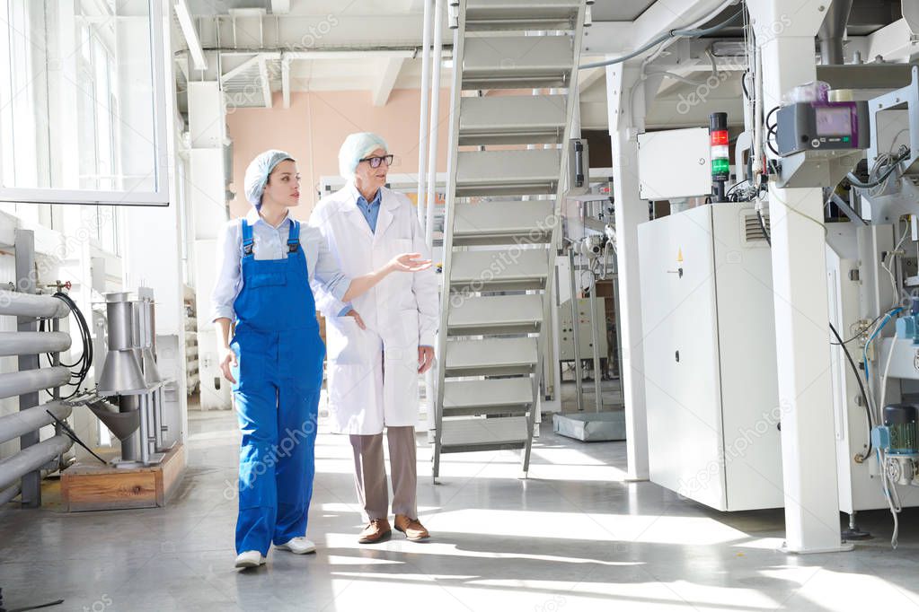 Full length portrait of young female worker giving tour of factory to senior woman, copy space
