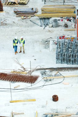 Kazı planlarını görüntülerken ve şantiyede çerçeve ve kablolarla dururken inşaat yöntemlerini tartışan hardhatlı ve yeşil yelekli mühendislerin doğrudan yukarıda