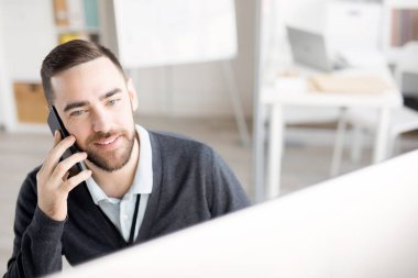 Modern ofiste masa başında çalışırken telefonla konuşan gülümseyen işadamının baş ve omuz portresi, kopya alanı