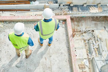 Yukarıda kask ve yelek li iki adamın yukarıdan vurulması, şantiyede beton levha üzerinde durup aşağıya bakıyor.