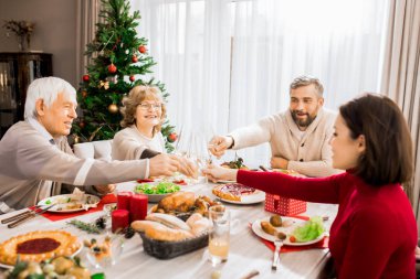 Büyük mutlu ailenin sıcak tonlu portresi noel yemeğinin tadını birlikte çıkarıyor ve şampanya bardaklarıyla kadeh kaldırıyor