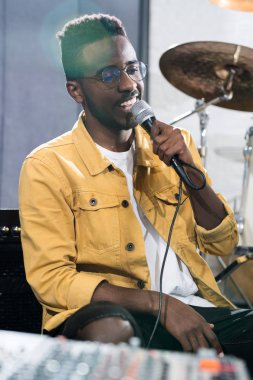 Stüdyoda müzik kaydı sırasında mikrofona şarkı söyleyen gülümseyen Afrikalı-Amerikalı adamın portresi
