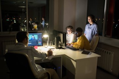 Karanlık ofiste gece çalışırken bilgisayar kullanan üç kişinin yan görünüm portresi, kopyalama alanı