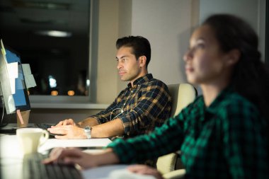 Karanlık ofiste geç saatlere kadar çalışan iki bilgisayar programcısının yan görünüm portresi, geceleri bilgisayar klavyesinde yazan adama odaklanın