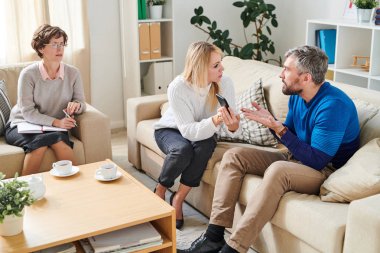 Sarı saçlı kızgın genç eş kanepede oturan ve psikoloji oturumunda psikiyatrist önünde hile için onu suçlarken kocasına metresi sms gösteren.