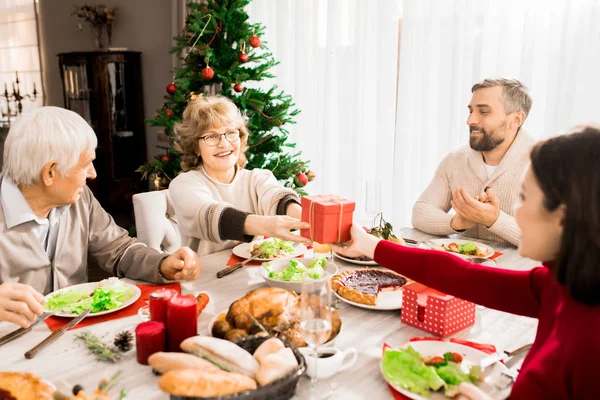 Büyük mutlu ailenin sıcak tonlu portresi noel yemeğinin tadını birlikte çıkarıyor, üst düzey kadına odaklanArak hediyeler veriyor