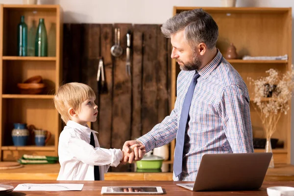 Ciddi kendine güvenen yakışıklı sakallı baba gömlek ve kravat mutfakta ayakta ve resmi gömlek küçük oğlu ile el sıkışma yapma