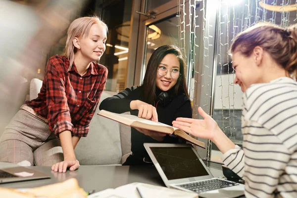 Gülümseyen genç kadın elinde bir ders kitabı tutan ve makaleişaret ve onlar kafede otururken sınıf arkadaşları ile tartışıyor