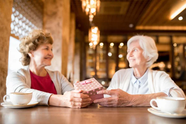 Yakın arkadaş doğum günü kutlarken kahve dükkanında masada oturan ve hediye kutusu veren kıvırcık saçlı gülümseyen çekici bayan