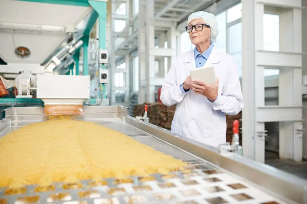 コンベアベルトで立ち 食品生産を制御するデジタルタブレットを使用して工場で働くシニア女性の肖像画をウエストアップ コピースペース — ストック写真