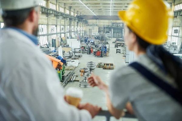 Back view of two workers looking at interior of factory workshop from above, copy space